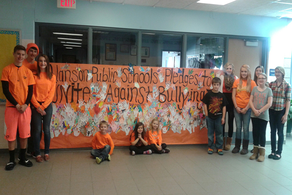 Alanson Public Schools students pose in front of the large poster created with handprints from the full student body to represent their unity against bullying. 