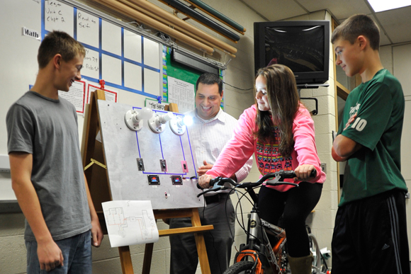 Freeland Public Schools students Trey Gleason, Jessica Kelsey, and Tyler McLaren, along with teacher Scott Harrison, test out their bike generator project.